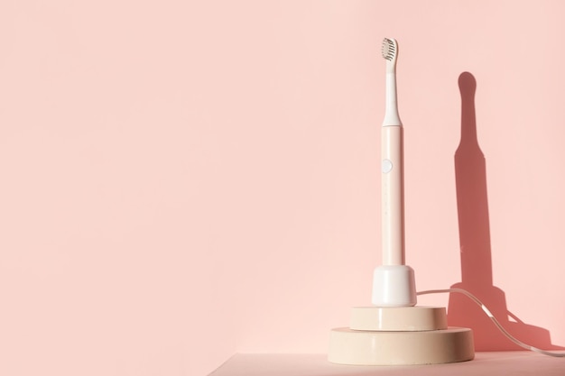 Nuevos suministros de cuidado dental de cepillo de dientes ultrasónico moderno en podio de cilindro sobre fondo rosa pastel o...