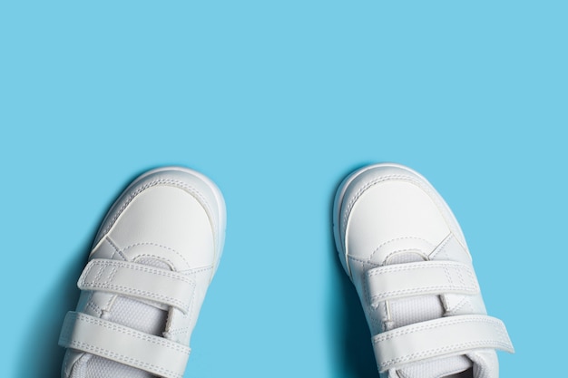 Nuevos zapatos deportivos blancos para niños o zapatillas de deporte sobre el fondo pastel azul claro.