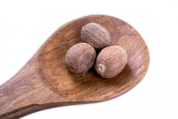 Nuez moscada entera en la cuchara de madera aislada en blanco