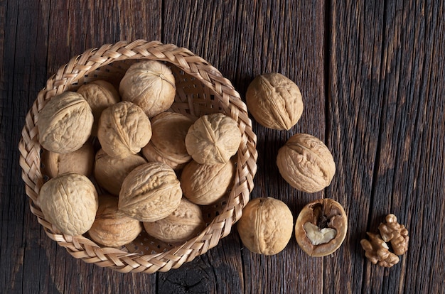 Nuez en un tazón y granos de nueces en la mesa de madera oscura, vista superior