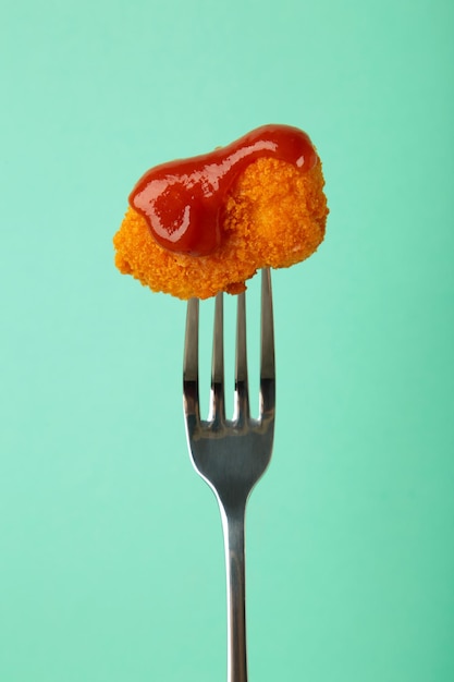 Foto nugget de frango com ketchup em um garfo em fundo de hortelã foto vertical