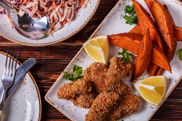 Nuggets de frango cozido caseiro, batata doce e salada de repolho em madeira escura