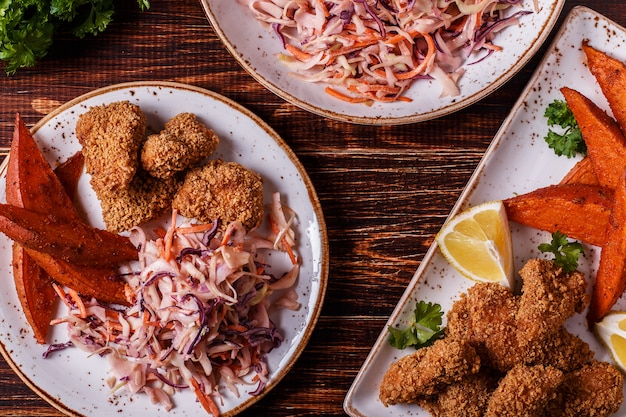 Nuggets de frango cozido caseiro, batata doce e salada de repolho em madeira escura