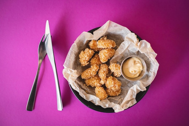 Nuggets de frango crocante com molho de queijo em um fundo roxo brilhante