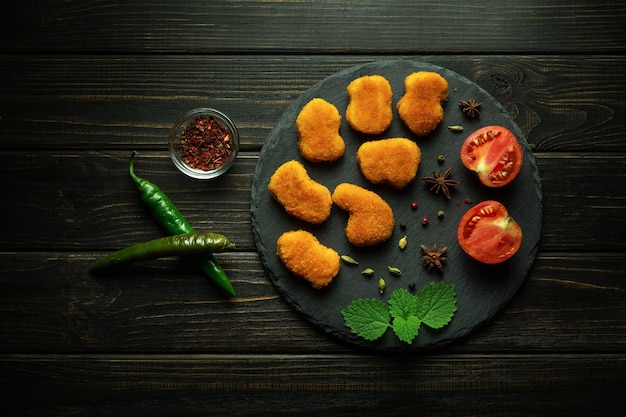 Nuggets de frango crocantes em uma prancha redonda com especiarias pimenta de caiena e tomates