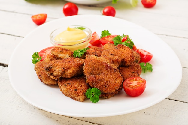 Nuggets de frango e molho no prato sobre uma mesa de madeira branca