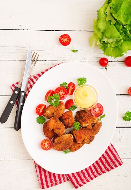 Nuggets de frango e molho no prato sobre uma mesa de madeira branca