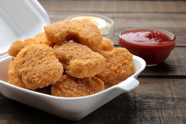 Nuggets de frango em uma caixa de entrega de comida com molho branco e vermelho sobre um fundo de madeira marrom. close-up de fast food