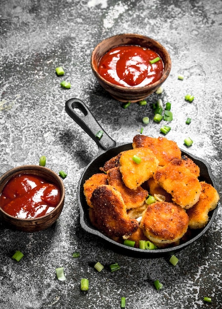 Nuggets de frango em uma frigideira com molho de tomate.