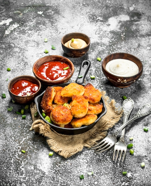 Nuggets de frango em uma panela com molhos diferentes.