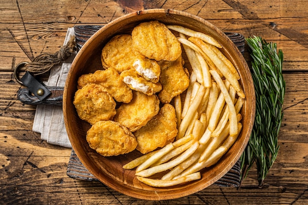 Nuggets de frango frito crocante com batatas fritas em placa de madeira Fundo de madeira Vista superior