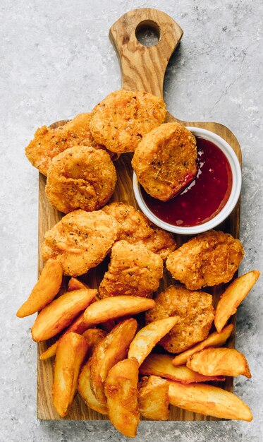 Nuggets fritos esfarelados com batata frita e uma tigela pequena de molho.