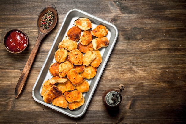 Nuggets de pollo en bandeja de acero con salsa.