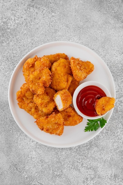 Nuggets de pollo crujientes con ketchup en un plato blanco sobre un fondo de hormigón gris