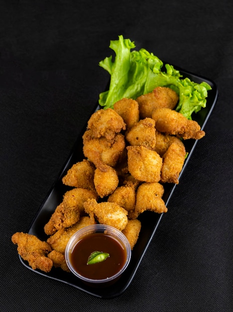 Foto nuggets de pollo frito natural con salsa bbq y lechuga decorativa.