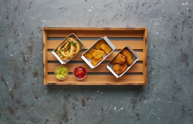 Nuggets de pollo frito con patas y pulpo crujiente en bandeja de madera, vista superior, espacio de copia. Concepto de comida callejera