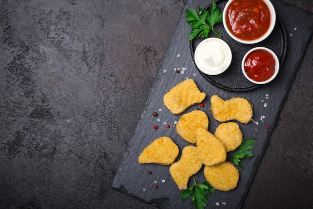 Nuggets de pollo fritos y crujientes con salsas populares en un fondo negro, espacio para copiar