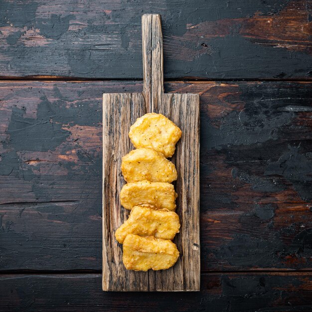 Nuggets de pollo fritos sobre fondo de madera oscura, con espacio para texto.