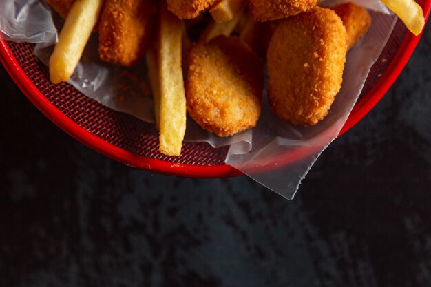 Foto nuggets de pollo en una olla roja con papas fritas y queso