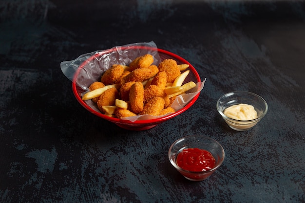 Nuggets de pollo en una olla roja con papas fritas y salsa bbq