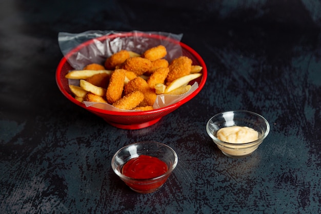 Nuggets de pollo en una olla roja con papas fritas y salsa bbq