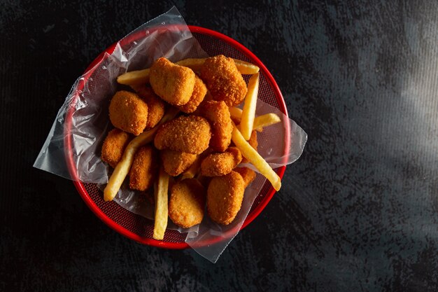 Nuggets de pollo en una olla roja con papas fritas