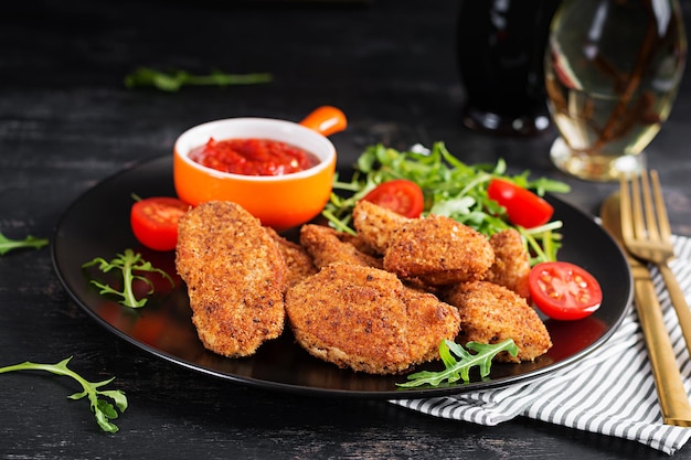 Nuggets de pollo y salsa en un plato negro sobre un fondo oscuro.