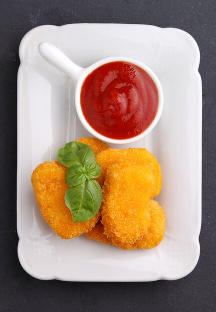 Nuggets de pollo con salsa de tomate decorados con albahaca en un plato blanco