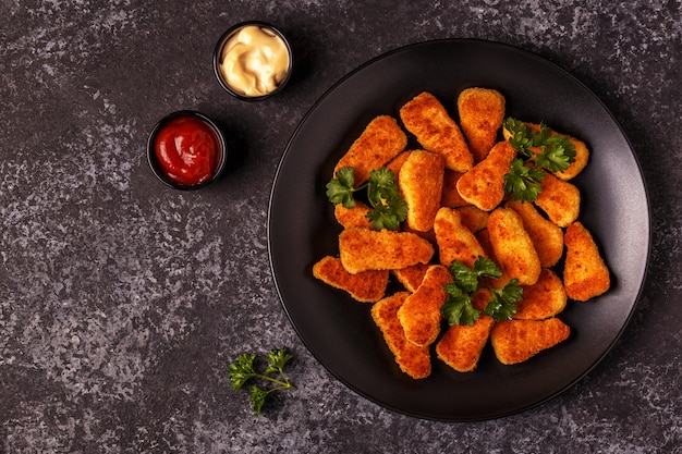 Nuggets de pollo con salsas sobre superficie oscura