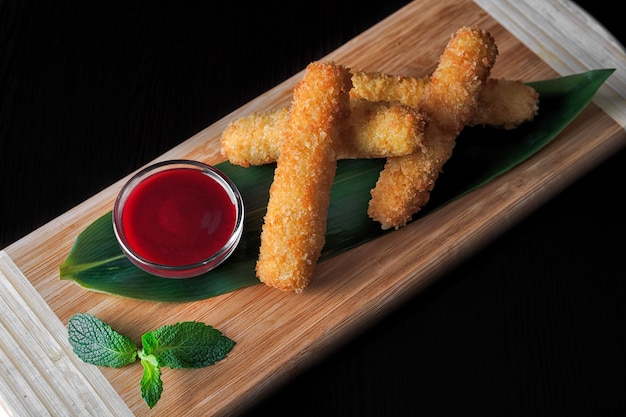 Nuggets de queso con salsa, sobre una tabla de madera con una hoja de bambú y menta, sobre un fondo negro