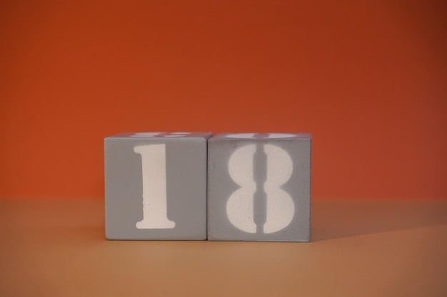 Número 18 en cubos grises de madera primer plano Concepto de fecha hora Concepto matemático Copiar espacio para texto o evento Números blancos 18 en bloques de construcción fondo naranja Cubos educativos Enfoque selectivo