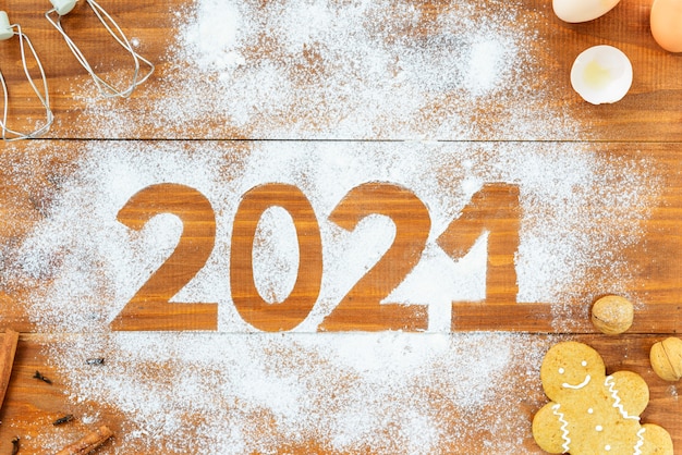 Número 2021 alrededor de harina, huevos, batir y especias en una mesa de madera marrón.