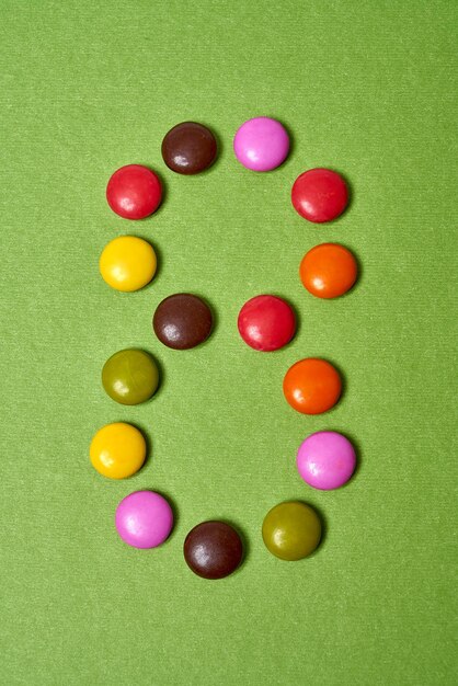 Número 8 escrito con caramelos de chocolate redondos de colores sobre fondo verde.