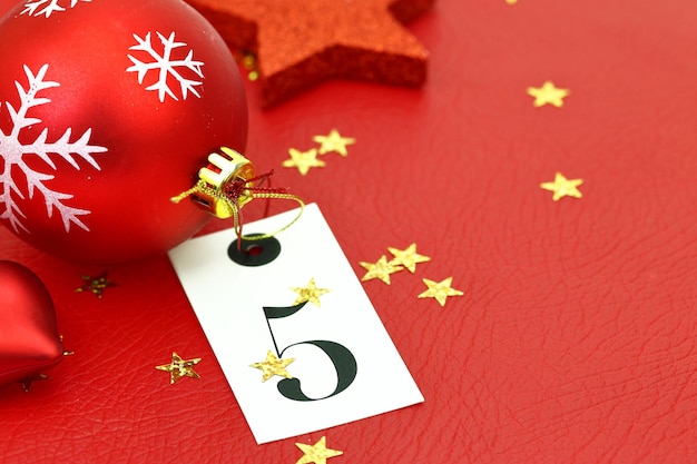 Número cinco na etiqueta e enfeites de Natal em fundo vermelho