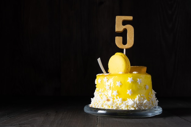 El número Cinco en un pastel amarillo para un aniversario o cumpleaños en una clave oscura