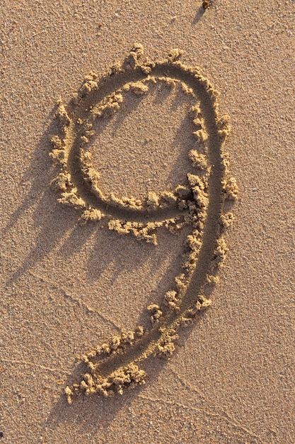 Número nove escrito em uma praia arenosa. Coleção de personagens escritos à mão.