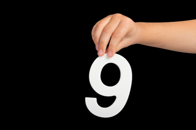Número nove na mão isolado no número de fundo preto na mão de uma criança em um fundo preto a ser