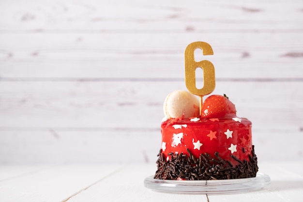 El número seis en un pastel de cumpleaños rojo sobre un fondo claro