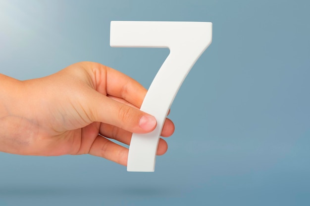Número siete en la mano sosteniendo el número blanco sobre fondo azul con el concepto de espacio de copia con número