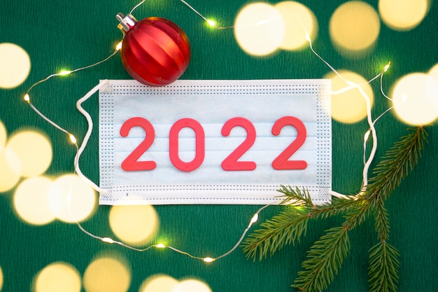 Los números 2022 se encuentran en una máscara médica sobre un fondo verde. Feliz año nuevo, Navidad y concepto de salud.