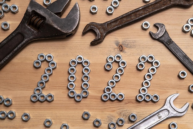 Los números 2022 están alineados con tuercas de metal sobre una mesa de madera junto a una variedad de llaves