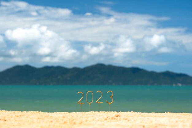 Foto números 2023 feliz año nuevo en una playa soleada con vistas a las olas y la isla vecina