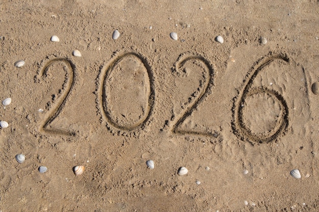 Los números 2026 están escritos a mano en la arena de la orilla del mar alrededor de la concha