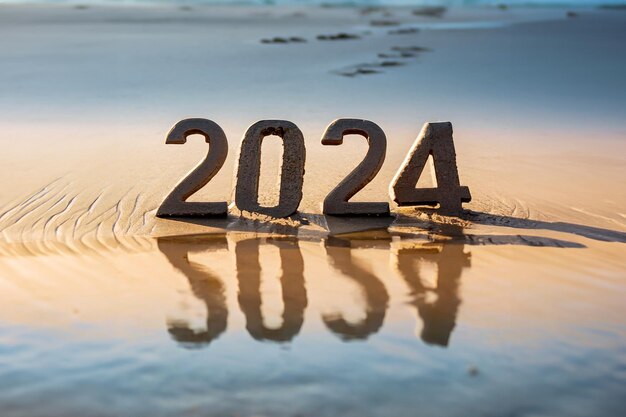 Números de Año Nuevo 2024 tipo 3D en la arena de una playa con reflejo entre las olas del mar