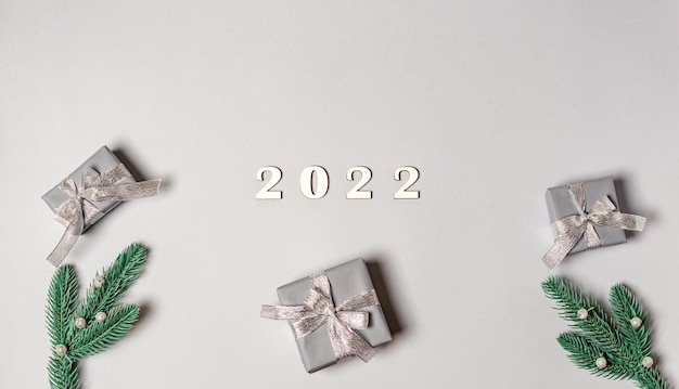 Números de madera 2022 con cajas de regalo, ramas de abeto sobre un fondo gris con lugar para el texto.