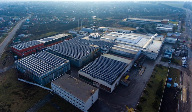 Numerosos painéis solares montados no edifício industrial aplicando uma área de telhado espaçosa para produzir energia limpa vista da área rural ao fundo