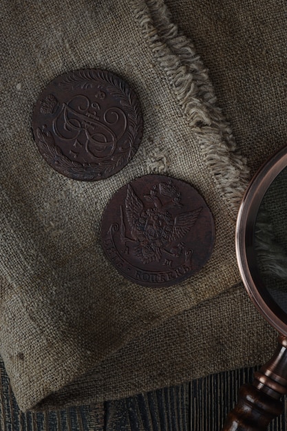 Numismatik. Alte Sammlermünzen und eine Lupe auf einem Holztisch. Dunkler Hintergrund. Ansicht von oben.