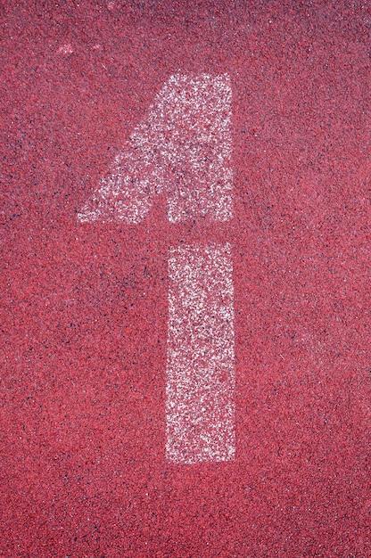 Nummer eins auf der Laufstrecke. Weiße Spurnummer auf roter Gummirennbahn, Textur der Rennstrecken im Stadion