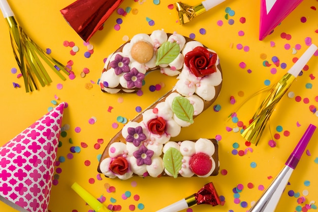 Nummer zwei Kuchen dekoriert mit Blumen, Macarons und Konfetti auf gelbem Grund
