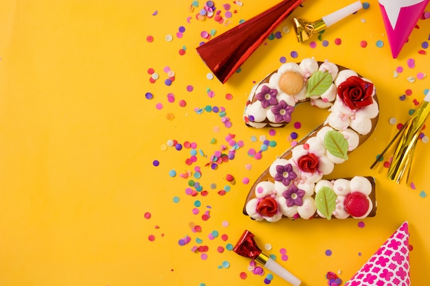 Nummer zwei Kuchen dekoriert mit Blumen, Macarons und Konfetti isoliert auf gelbem Hintergrund Kopieren Sie Platz